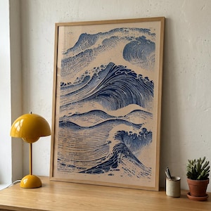 Puede incluir: Una lámina de arte enmarcada que presenta una ilustración en tinta azul oscuro de olas estilizadas sobre un fondo beige claro. La obra está dentro de un marco de madera clara y muestra un intrincado trabajo de líneas que representa el oleaje.