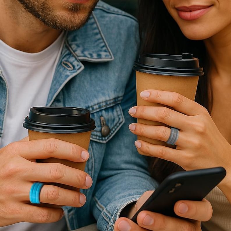 May include: A couple holding coffee cups, each wearing a silicone ring. One ring is blue, the other is gray. The rings are approximately 0.3 inches wide. The couple is also holding a smartphone.