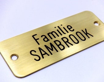 May include: A gold-colored metal nameplate with the text "Familie SAMBROOK" engraved in black.