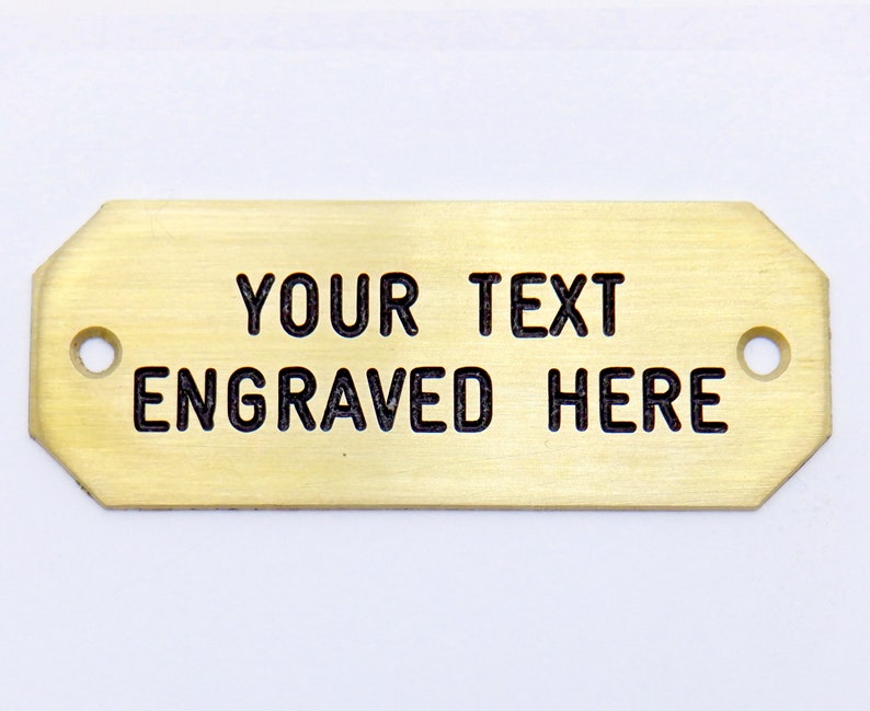 May include: A gold-colored metal rectangular tag with rounded corners and two holes. The tag has the text "YOUR TEXT ENGRAVED HERE" engraved on it.