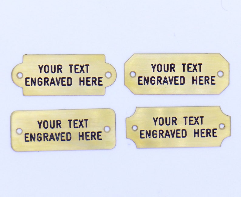 May include: Four gold-colored metal tags with rounded corners and holes. Each tag has the text "YOUR TEXT ENGRAVED HERE" in black.