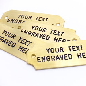 May include: Four brass tags with rounded corners and two holes. The tags are stacked on top of each other. The text "YOUR TEXT ENGRAVED HERE" is engraved on each tag.