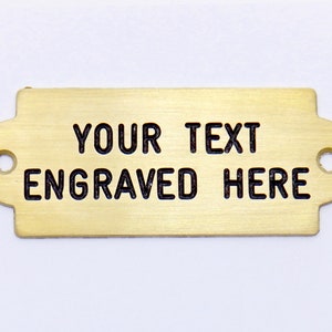 May include: A gold-colored metal plaque with rounded edges and two holes. The text "YOUR TEXT ENGRAVED HERE" is engraved in black lettering.