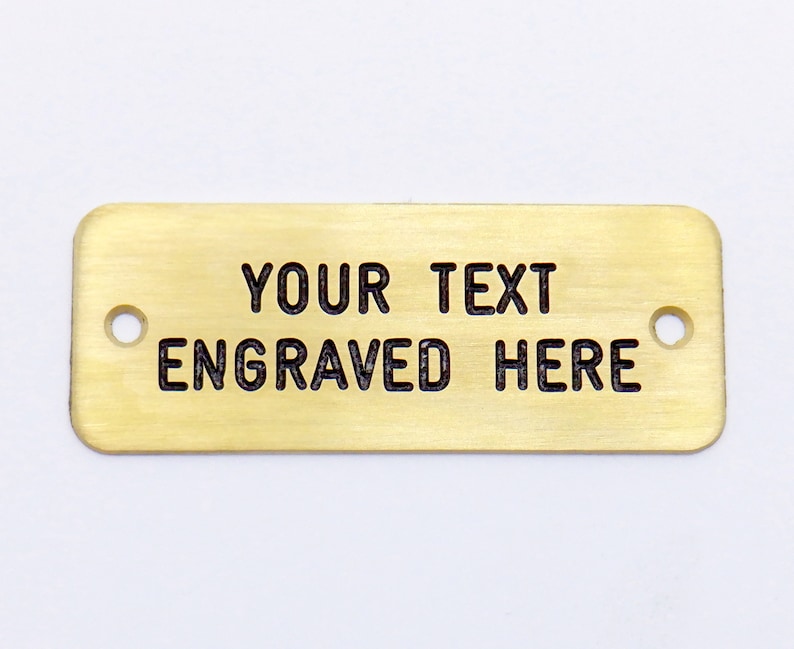 May include: A gold-colored rectangular metal tag with two holes. The tag has the text "YOUR TEXT ENGRAVED HERE" engraved on it.