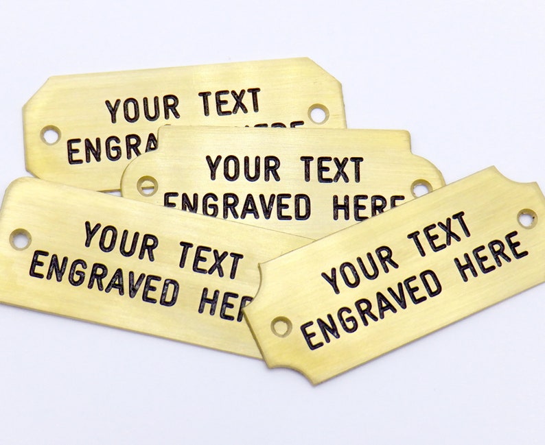 May include: Five brass tags with rounded corners and two holes. The tags are blank except for the text "YOUR TEXT ENGRAVED HERE" on each tag.