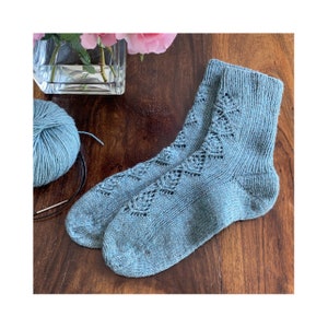 May include: A pair of blue knitted socks with a lacy pattern. The socks are lying on a wooden surface.