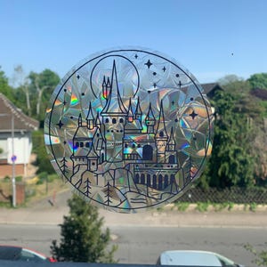 Könnte beinhalten: Ein runder Aufkleber mit einer schwarzen Umrandung eines Schlosses mit einem Vollmond und Sternen im Hintergrund. Der Aufkleber hat eine holografische, irisierende Oberfläche.