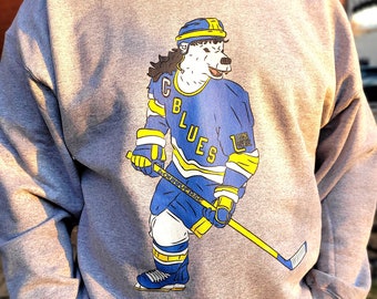 May include: A gray sweatshirt with a graphic of a hockey player wearing a blue and yellow jersey with the text "CB Blues" on the front. The player is a polar bear with a yellow helmet and a hockey stick.