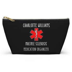 May include: Black zippered cosmetic bag with the text "CHARLOTTE WILLIAMS" above a red medical symbol and the words "MULTIPLE SCLEROSIS MEDICATION ORGANIZER". The bag has a gold zipper.
