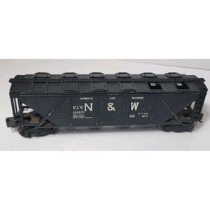 May include: A black model train car with the text "Norfolk and Western" and the letters "N & W" on the side. The model train car has a series of rectangular openings along the top and is sitting on a white surface.