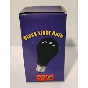 Op de afbeelding: Een zwarte gloeilamp in een paarse doos. De doos heeft de woorden "Black Light Bulb" in het geel en het wattage "75 W" in het rood. De gloeilamp is zwart met een zilveren voet.