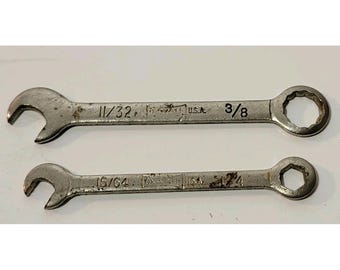 May include: Two vintage metal wrenches. The top wrench is marked "11/32" and "3/8". The bottom wrench is marked "15/64" and "1/4". Both wrenches are stamped "U.S.A."