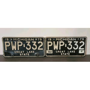 Puede incluir: Dos placas de matrícula vintage de Michigan de 1979. Ambas placas son negras con letras y números blancos. Las placas dicen "PWP 332" y "GREAT LAKE STATE". Una placa tiene impreso "MAR" y "81".