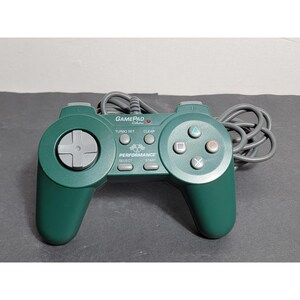 May include: A dark green wired video game controller featuring a grey directional pad, four action buttons with geometric symbols, and two shoulder buttons. The centre console displays the text GAMEPAD Colors, PERFORMANCE, SELECT, START, TURBO SET, and CLEAR.