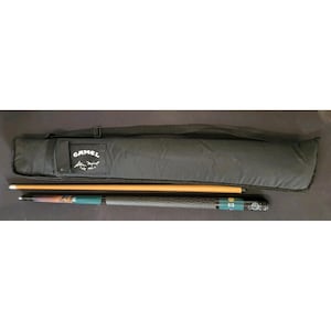 Könnte beinhalten: Ein zweiteiliges Billardqueue mit einem hellen Holzoberteil und einem dunkelgrünen sowie schwarzen Unterteil mit strukturiertem Griff, dazu eine schwarze Stofftasche mit verstellbarem Schultergurt und dem aufgedruckten Camel-Logo.