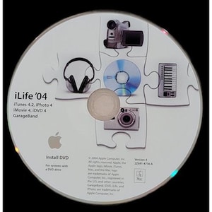 May include: A white iLife '04 install DVD with a puzzle design featuring a camcorder, headphones, a CD, a camera, and a keyboard. The Apple logo is visible, along with the text "Install DVD" and software names.
