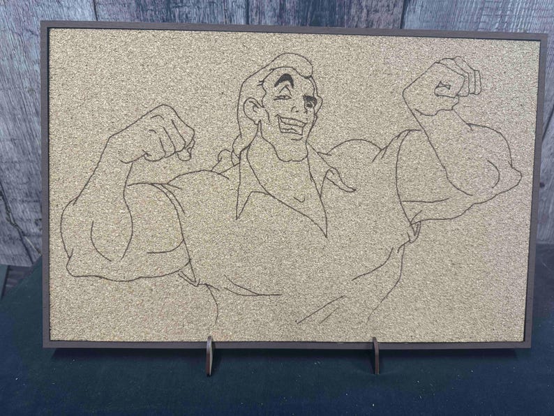 Puede incluir: Un tablero de corcho enmarcado con un dibujo lineal de un hombre musculoso flexionando sus brazos. La obra de arte est&aacute; en un marco oscuro y est&aacute; sostenida por un soporte met&aacute;lico. El fondo es de color marr&oacute;n claro.