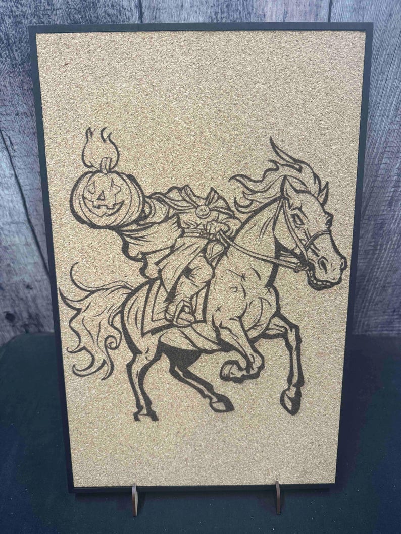 Puede incluir: Imagen en negro y marr&oacute;n del Jinete sin Cabeza sobre un tablero de corcho. La ilustraci&oacute;n representa al Jinete sin Cabeza montado a caballo, sosteniendo una linterna de calabaza. La obra est&aacute; enmarcada en negro y se mantiene en pie con un peque&ntilde;o soporte.