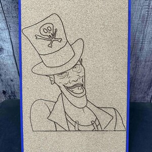 Puede incluir: Una obra de arte en tablero de corcho con marco azul presenta un dibujo lineal detallado de un personaje de dibujos animados. El personaje lleva un sombrero de copa con un emblema de calavera. La obra est&aacute; montada sobre un soporte de madera.