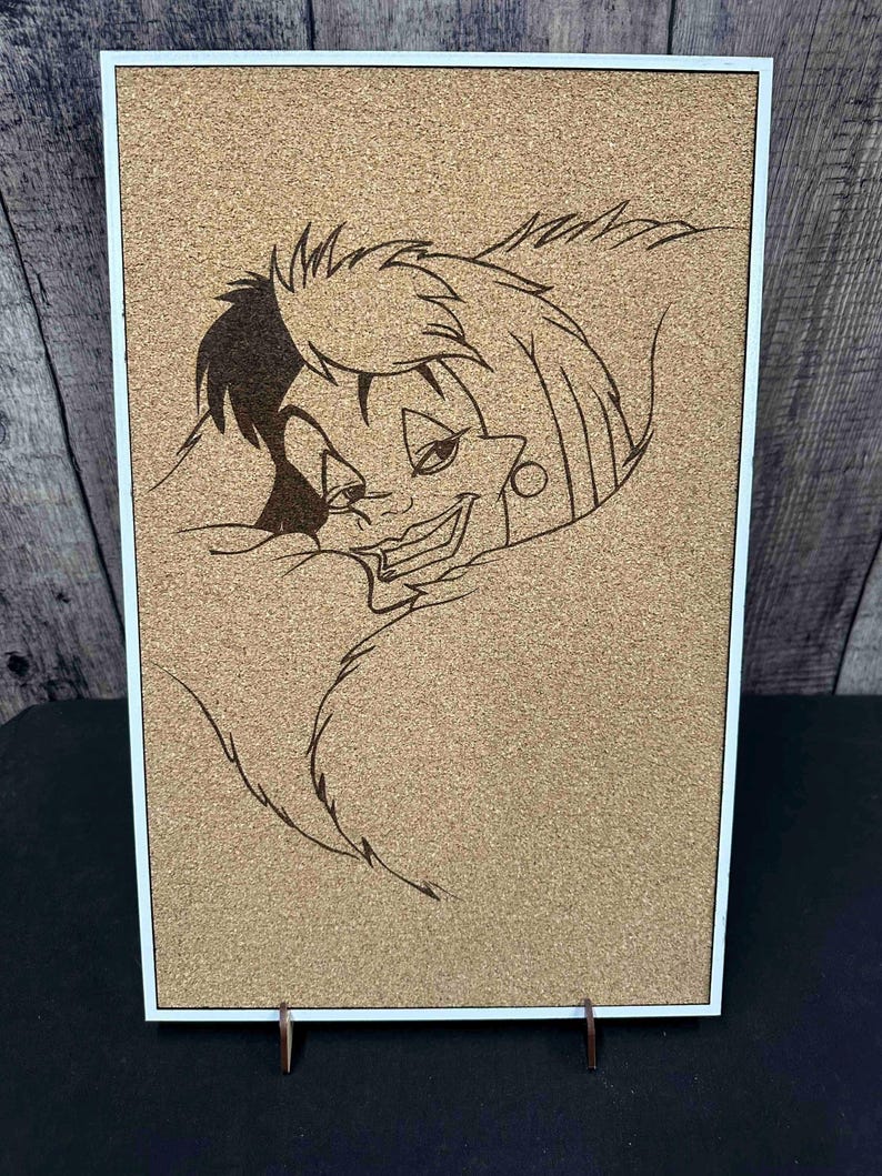 Puede incluir: Un tablero de corcho con marco blanco que presenta una imagen quemada en madera de un personaje de dibujos animados con cabello blanco y negro y una sonrisa siniestra. La obra de arte se exhibe en un soporte de madera.