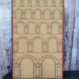 May include: A rectangular corkboard with a red border features a laser-cut design of arched columns. The design is repeated in multiple rows, creating a classical architectural pattern. The corkboard is ideal for displaying notes or photos.