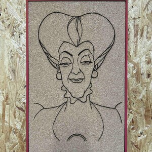 Puede incluir: Un corcho enmarcado con un dibujo lineal negro de una mujer con una expresi&oacute;n severa y un peinado grande. El marco es de color rojo oscuro. El fondo es un corcho marr&oacute;n claro.