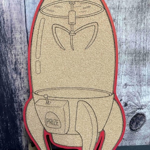 May include: A rocket-shaped corkboard with a red outline. The design includes a claw machine graphic at the top and a "PRIZE" box on the side. The corkboard is ideal for displaying notes or photos.