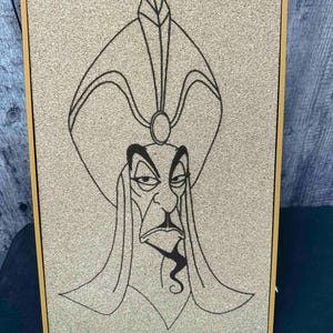 Puede incluir: Un corcho enmarcado con un dibujo lineal negro de un personaje con un tocado alto y una barba larga y puntiaguda. El marco es de color marr&oacute;n claro y el fondo es de color beige claro.