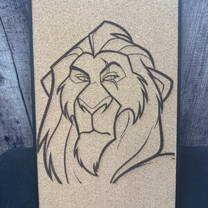 Puede incluir: Un corcho enmarcado con un dibujo lineal negro de la cabeza de un le&oacute;n. La cara del le&oacute;n est&aacute; detallada con una melena, ojos y nariz. El marco es negro y el corcho es de color marr&oacute;n claro.