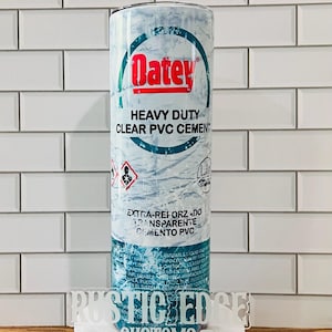 May include: A cylindrical tumbler featuring the "Oatey" logo in red, with the words "HEAVY DUTY CLEAR PVC CEMENT" in black. The design includes hazard symbols and text in English and Spanish. The tumbler is on a white surface.