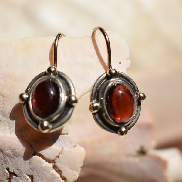 Oval Garnet cabochon set in a polished silver bezel setting and centered on a solid silver disc with blackened detail.