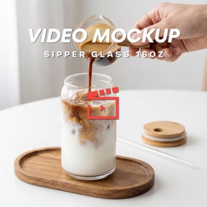 Puede incluir: Un vaso transparente para beber con tapa de madera y pajita, lleno de café helado y leche. Se vierte café en el vaso desde un pequeño recipiente de vidrio. Se muestra el texto "VIDEO MOCKUP SIPPER GLASS 16OZ".