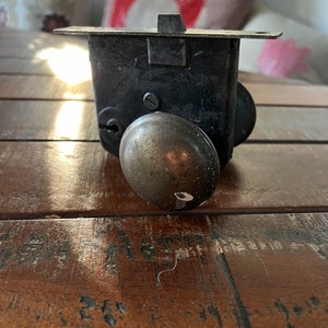May include: Antique black metal door lock with a brass knob. The lock has a rectangular body with a keyhole and a protruding latch. The knob is round and shows signs of wear. The lock is likely from a vintage door.