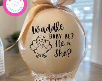 May include: A round, beige balloon featuring a black graphic of a turkey and the text Waddle BABY BE? He OR She? The balloon is topped with a beige satin ribbon bow and decorated at the base with white tissue paper featuring gold polka dots.