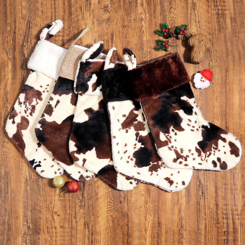 May include: A collection of Christmas stockings with a cowhide pattern in shades of brown, black, and white. Each stocking has a different cuff color, including white, tan, and brown. Festive holiday decor.