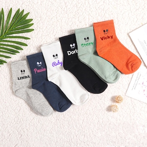 May include: Six pairs of colorful ankle socks with a cartoon Mickey Mouse head and a name embroidered on each sock. The names are Linda, Paula, Ruby, Dori, Stacey, and Vicky.