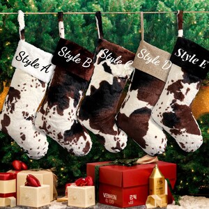 May include: Five Christmas stockings with a cowhide pattern hang against a backdrop of a Christmas tree. Each stocking has a different style, labeled A through E. The stockings are white, brown, and black, with a faux fur texture.