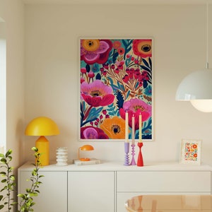 May include: A framed print of a colorful floral illustration with pink, red, orange, and yellow flowers. Three candlesticks with candles are in front of the print on a white countertop.