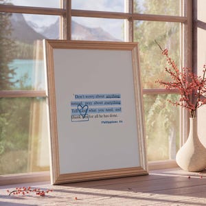 May include: A framed print with a quote from Philippians 4:6. The quote reads "Don't worry about anything instead, pray about everything. Tell God what you need, and thank Him for all He has done." The print is hanging on a wall with a window behind it.
