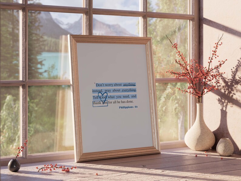 May include: A framed print with a quote from Philippians 4:6. The quote reads "Don't worry about anything instead, pray about everything. Tell God what you need, and thank Him for all He has done." The print is hanging on a wall with a window behind it.