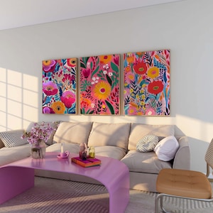 May include: Three colorful floral paintings with pink, red, yellow, and blue flowers on a white background hang above a beige sofa with pillows. A pink coffee table sits in front of the sofa.