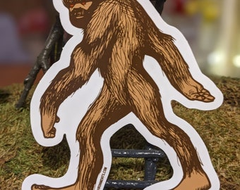 May include: A brown and orange Bigfoot sticker with a white background. The sticker shows a Bigfoot walking with its arms outstretched. The sticker has the text "zenvybonments.com" on the bottom.