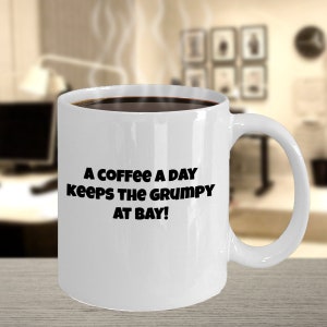 Puede incluir: Taza de café de cerámica blanca con texto negro que dice "A coffee a day keeps the grumpy at bay!"