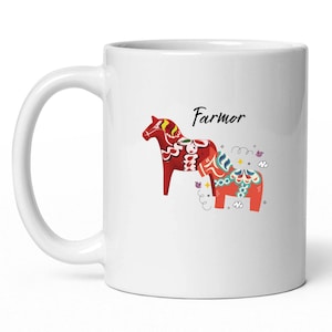 May include: White ceramic mug featuring two stylized red Dala horses with intricate patterns. The word "Farmor" is written above the horses in black script. The mug has a curved handle.