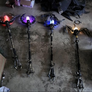 May include: Four fantasy-themed staffs with intricate designs. Each staff features a unique glowing orb at the top, with colors including red, purple, and blue. The staffs have detailed metalwork and claw-like structures at the base.