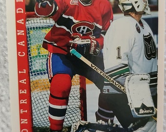 May include: A hockey trading card featuring John Leclair, a left wing for the Montreal Canadiens. He is wearing a red, white, and blue jersey with the team's logo. He is holding a hockey stick and is in the process of shooting the puck. The card is from the Score series.