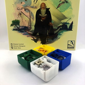 May include: A yellow, green, white and blue box set for the board game Darwin's Journey. The box set includes four small boxes, each with a different colour and containing game pieces. The game box is in the background and features an illustration of Charles Darwin on a ship.
