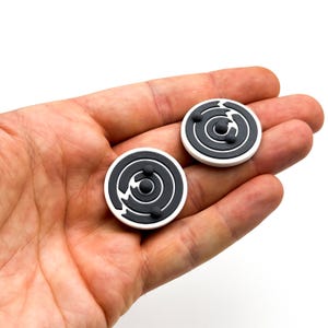 May include: Two black and white round decorative coasters with a swirling pattern and three black dots in the center.