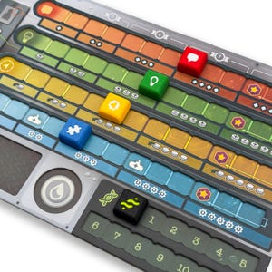 Könnte beinhalten: Ein Brettspiel mit farbenfrohem Design, das verschiedene farbige Bahnen und Würfel zeigt. Die Würfel sind rot, grün, gelb, blau und schwarz, jeder mit einzigartigen Symbolen. Das Spielbrett hat eine metallisch-graue Oberfläche mit nummerierten Abschnitten.