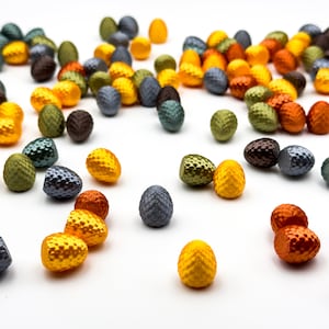 May include: A collection of small, colorful, textured eggs in shades of green, yellow, orange, and gray. The eggs are scattered on a white surface.